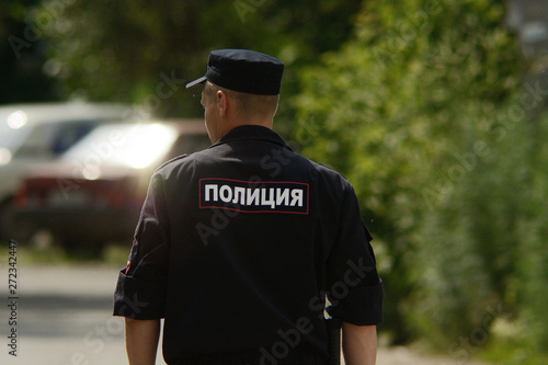 Russian policeman patrols street of provincial town. Man in police uniform go in direction of russian cars. Inscription "police" on russian language on back. Russia, Barnaul, 08 July, 2014.