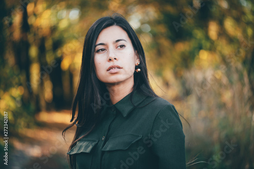 Female beauty portrait surrounded by vivid foliage. Dreamy beautiful girl with long natural black hair on autumn background with colorful leaves in bokeh. Inspired girl enjoys nature in autumn forest.