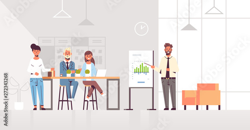 businessman presenting financial graph on flip chart to businesspeople team at conference meeting training presentation concept modern co-working space office interior full length horizontal