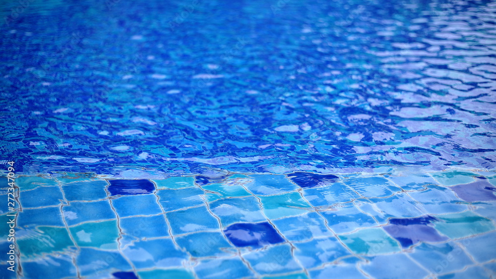 Fototapeta premium shallow wadding pool water in swimming pool. pool design with small ceramic tiles. repeating dark deep blue tiles dotted lighter shade of blue floor tiles. deeper level in the background.