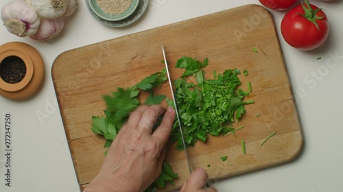 Woman's hands chopping a bunch of parsley on a wooden board