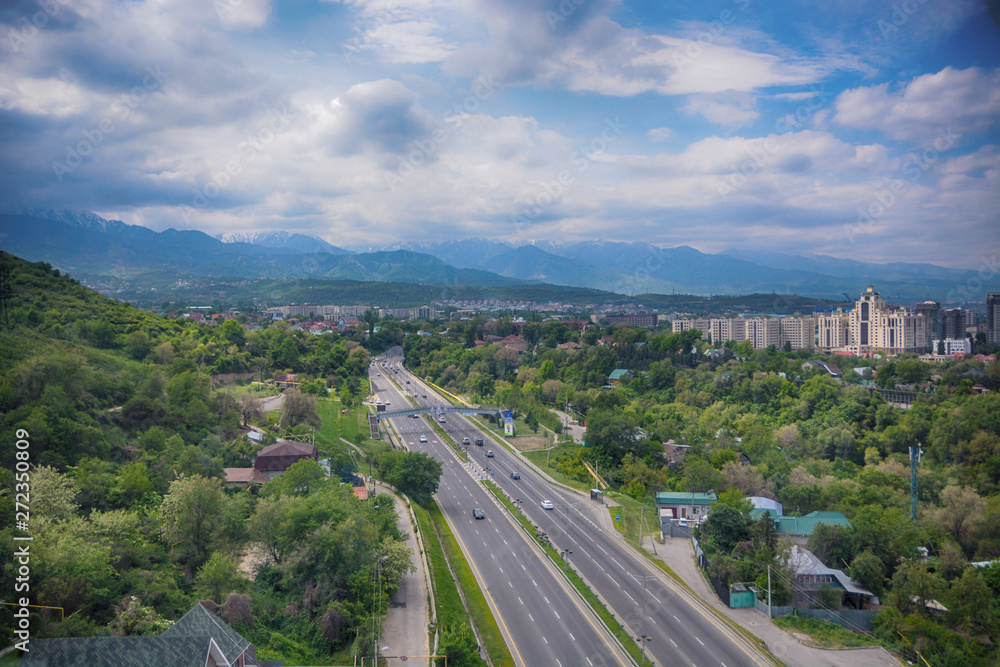 Panoramic view of the city of Almaty, with road, industrial zone, mountains and sky with clouds. Viewed from Kok tobe, Kazakhstan.