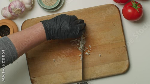Hands with black sanitary PVC gloves, chopping a garlic on a wooden board.