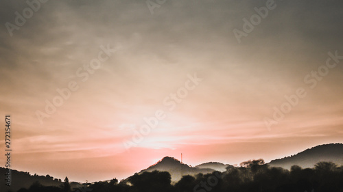 Sunset landscape with orange sky, silhouettes of mountains, hills and trees and lake
