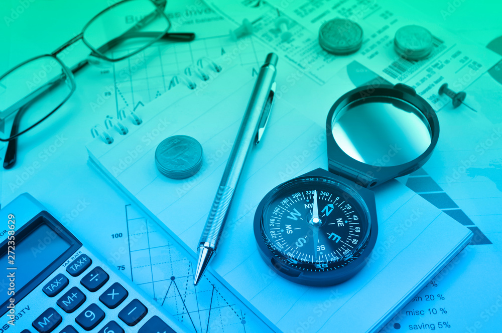 Blue compass, pen, coin, notebook, calculator, glasses on financial graph, Business investment concept Blue compass, pen, coin, notebook, calculator, glasses on financial graph, Business investment concept
