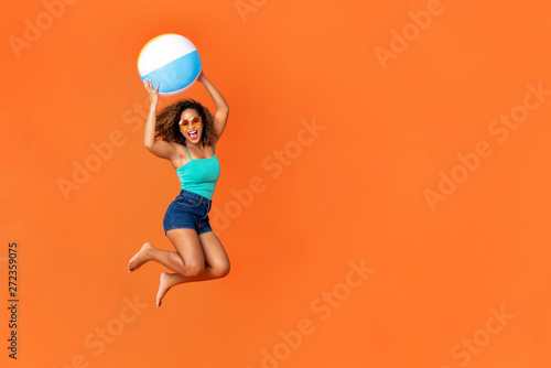 Young energetic African American woman holding beach ball and jumping