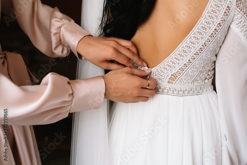 Bridesmaid preparing bride for wedding day. Bridesmaid helping bride fasten lacing her wedding white dress before ceremony. Luxury bridal dress close up. Wedding morning moments details concept