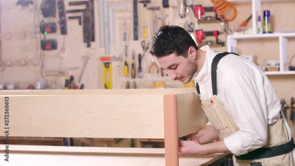 Concept of business and manufacture. Young man in the workshop assembles furniture Concept of business and manufacture. Young man in the workshop assembles furniture