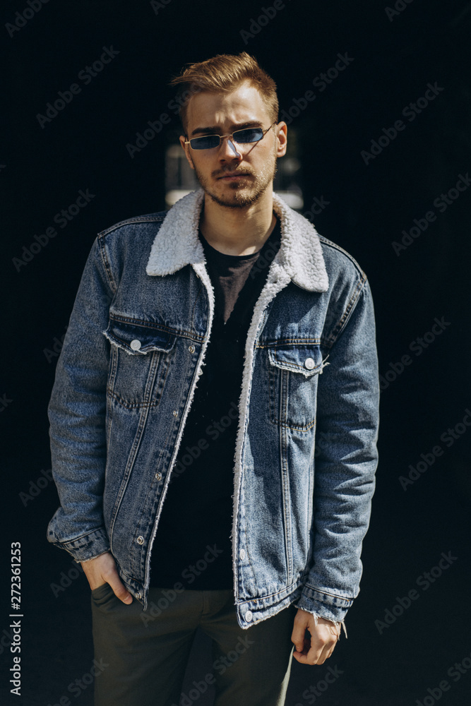 Portrait of young man in blue jeans jacket with sunglasses outdoor on dark background. Portrait of young man in blue jeans jacket with sunglasses outdoor on dark background.