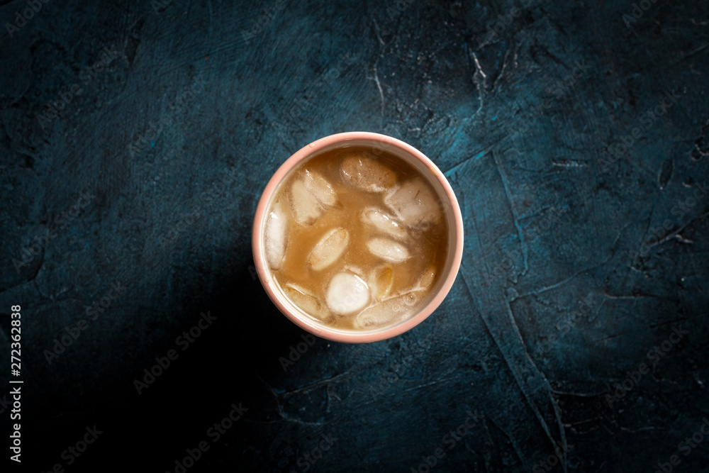 Coffee with ice and milk in a glass on a dark blue stone background. Concept cooling drink, thirst, summer, ice, nightlife, club. Flat lay, top view Coffee with ice and milk in a glass on a dark blue stone background. Concept cooling drink, thirst, summer, ice, nightlife, club. Flat lay, top view