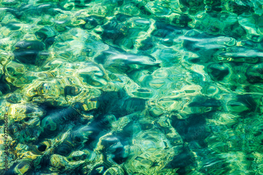 Transparent turquoise sea surface with sun glare, background. Close-up. Space for text. Transparent turquoise sea surface with sun glare, background. Close-up. Space for text.