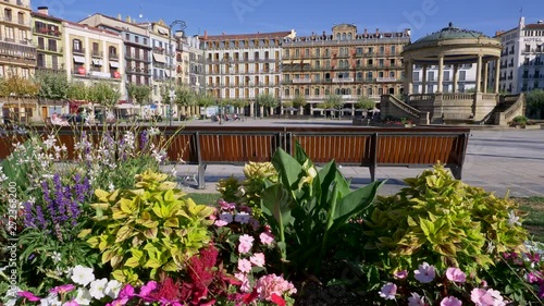 Pamplona, Spain. Bright colored flowers by a bench on a Plaza del Castillo. Lifting shot over flowers to get a wide view of the place. 4K photo