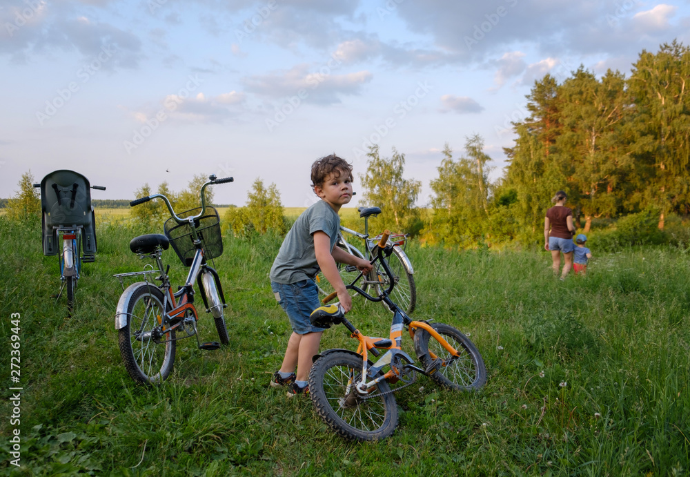 Obraz premium family summer bike ride.the boy holds the bike, my mother leads the younger brother in the direction of the forest by the hand. Parking paddles in nature