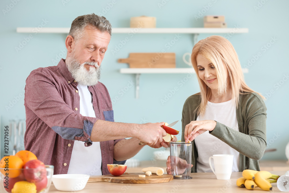 Happy elderly couple preparing smoothie in kitchen Happy elderly couple preparing smoothie in kitchen