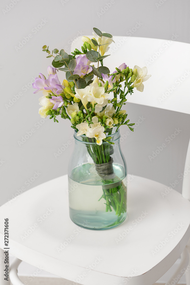 Vase with beautiful freesia flowers on chair against light background