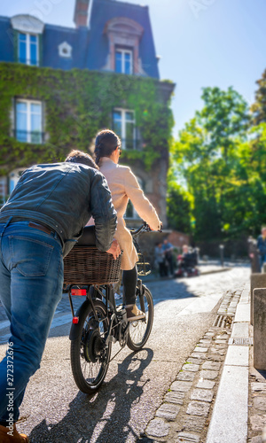 Man pushes bicycle with girl to the hill helping her ride up the street in Montmartre