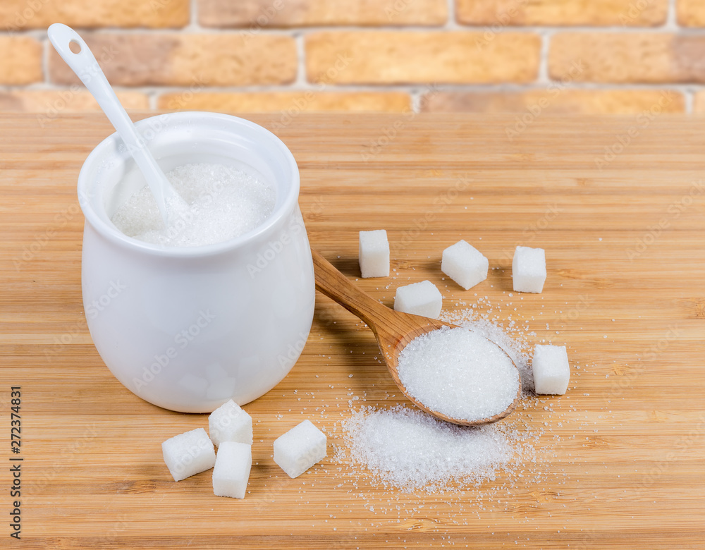 White sugar in sugar-bowl, wooden spoon and sugar cubes White sugar in sugar-bowl, wooden spoon and sugar cubes
