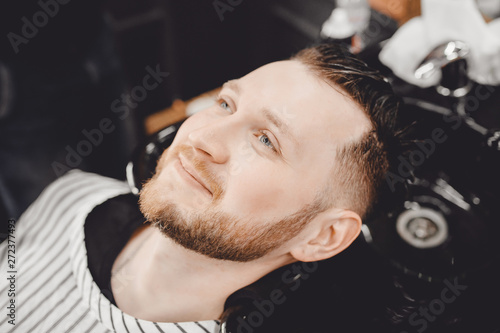 Male client washes his hair barber shop and smiles, stylish styling