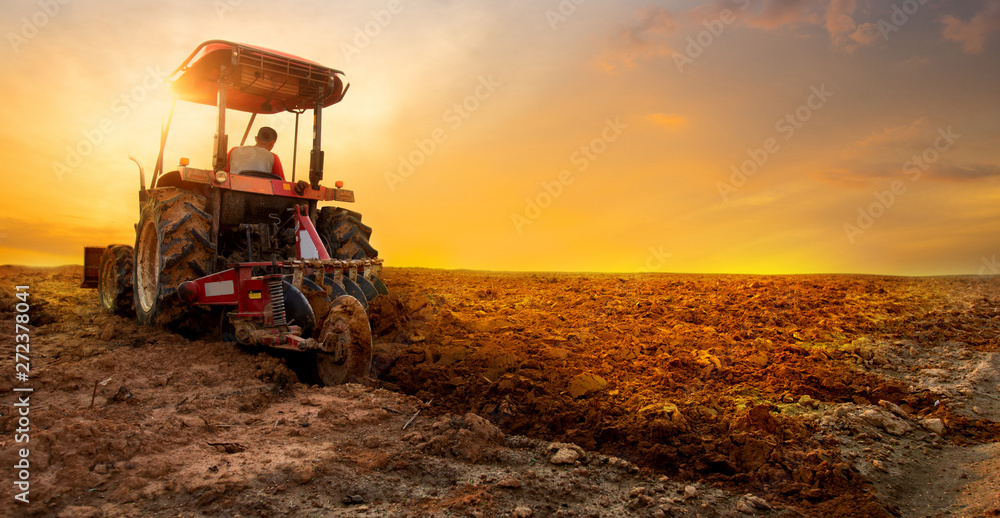 Naklejka premium tractor is preparing the soil for planting over sunset sky background