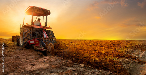 Fototapeta tractor is preparing the soil for planting over sunset sky background