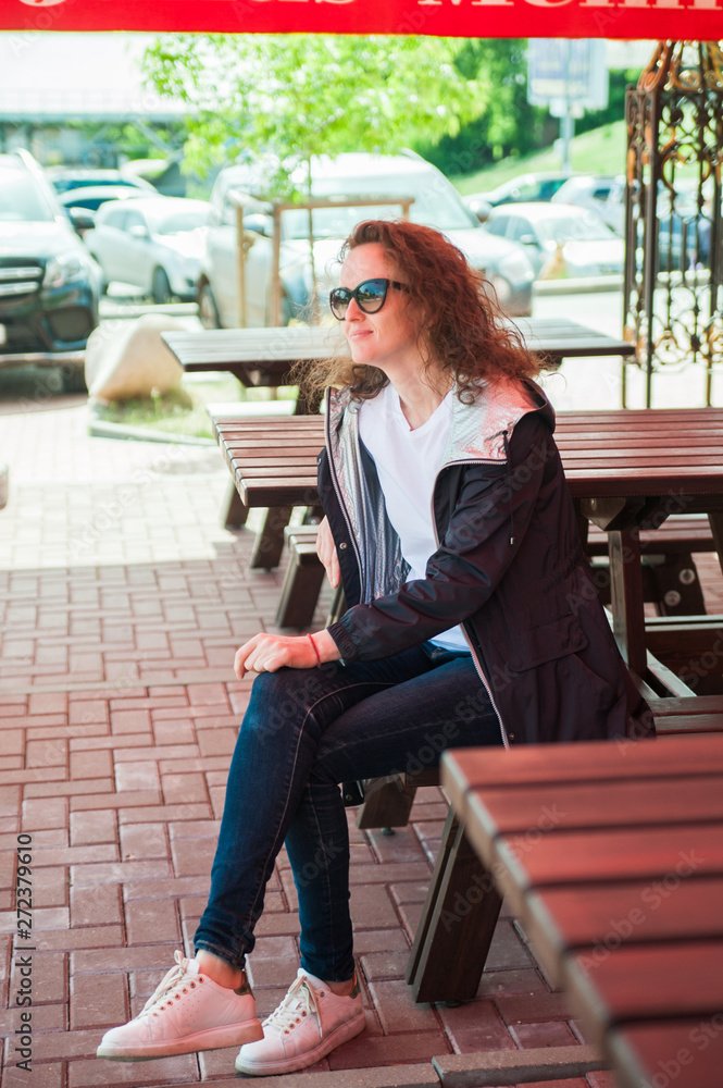 Outdoor portrait of a young beautiful curly woman in sunglasses posing on the street. Sunny day. City lifestyle.