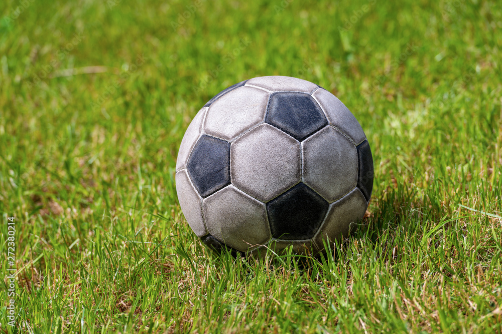 Close-up of an old leather soccer ball on green grass, football sport concept - obrazy, fototapety, plakaty 