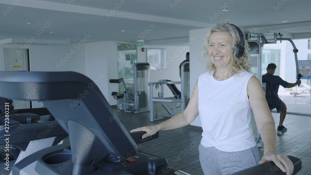 senior woman is engaged on a treadmill in the gym. blond female listens to music with headphones on the treadmill senior woman is engaged on a treadmill in the gym. blond female listens to music with headphones on the treadmill