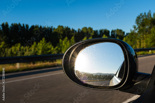 Left oval mirror car highway reflection on a blue sunny sky sun flare shining