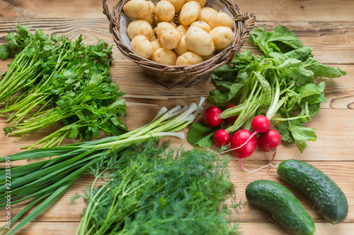 Fresh raw organic vegetables: potatoes, radishes, green onions, cucumbers on a wooden background.
