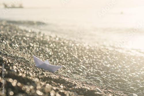 Paper boat lies on the seafront at sunrise.