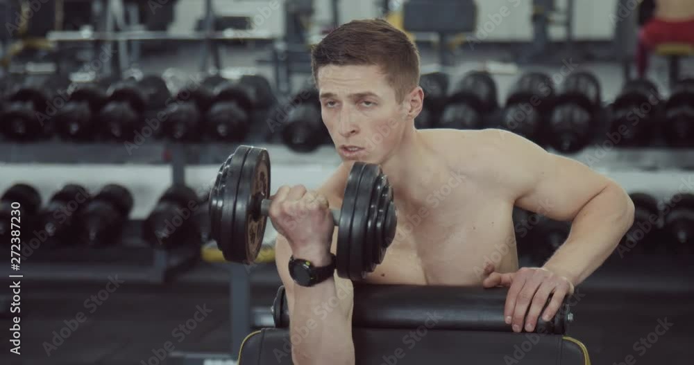 Handsome man doing biceps lifting barbell on bench in a gym Handsome man doing biceps lifting barbell on bench in a gym