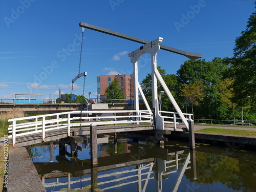 White woorden drawbridge over ring canal zuidplaspolder with train station nieuwerkerk on the background and bridge reflecting on water photo