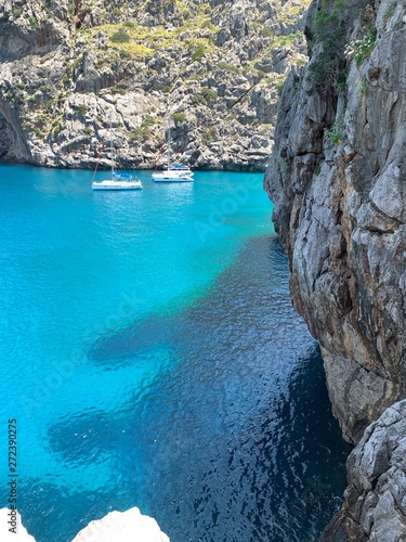 Beautiful turquoise blue ocean water on the rock coastline with small sailing boats on a nice vacation day. Perfect summer travel location in Canyon de la Calobra, Torrent de Pareis, Mallorca, Spain