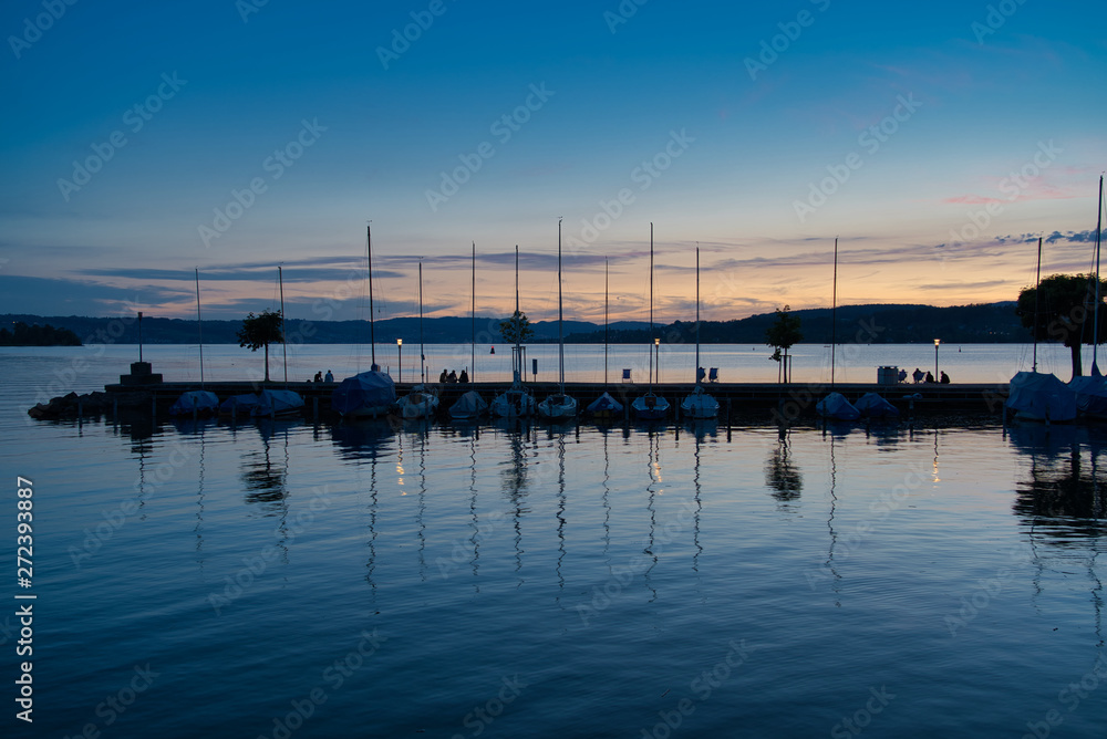 Menschen am Pier vor Segelschiffen und bei Sonnenuntergang