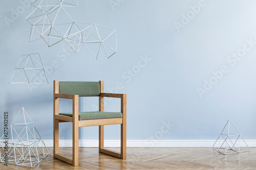 Minimalistic and modern interior of open space with design green armchair, triangle geometric sculptures. Gray background walls, brown wooden parquet. Abstarct concept of room.  Template.