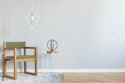 Minimalistic and modern interior of open space with design green armchair, stylish lamps and white coffee table. Gray background walls, brown wooden parquet. Concept of room. Template. Copy space.