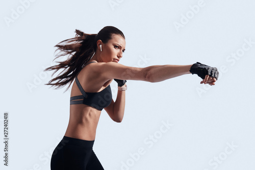 Fototapeta Naklejka Na Ścianę i Meble -  Fighting. Attractive young woman boxing while standing against grey background