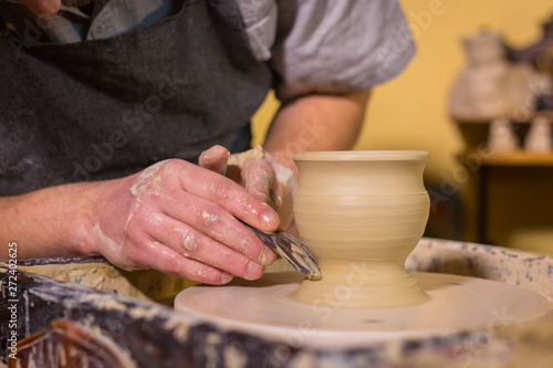 Professional potter carving mug with special tool in pottery workshop