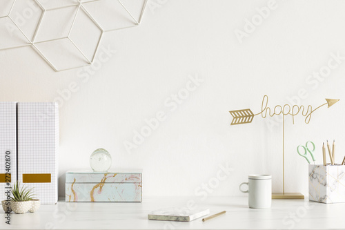 White and stylish home interior with design office accessories, notes, boxes, pencils and air plants. Gold happy sign. Cozy home office decor. Minimalistic concept. Template. Copy space. White walls.