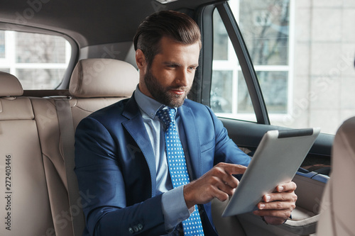 Using modern technologies. Young confident and stylish businessman in formal wear is working on digital tablet while sitting on the back seat of his car. © Friends Stock