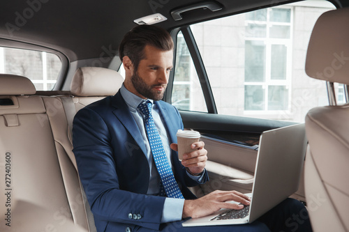 Focused on work. Busy young businessman in formal wear working on laptop and drinking hot coffee while sitting in his car. © Friends Stock
