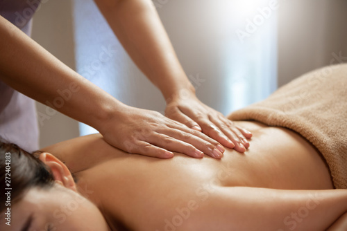 Masseuse doing massage on Asian female body in the spa salon.