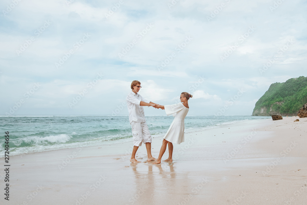 Girl and man in white clothes walking on white beach in Bali and holding hands