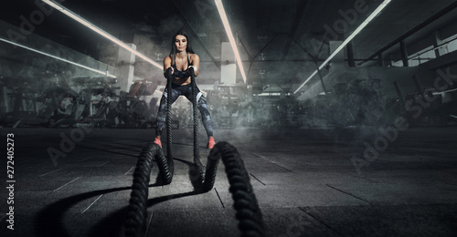 Sport backgrounds. Powerful attractive muscular woman fitness trainer do battle workout with ropes at the gym.