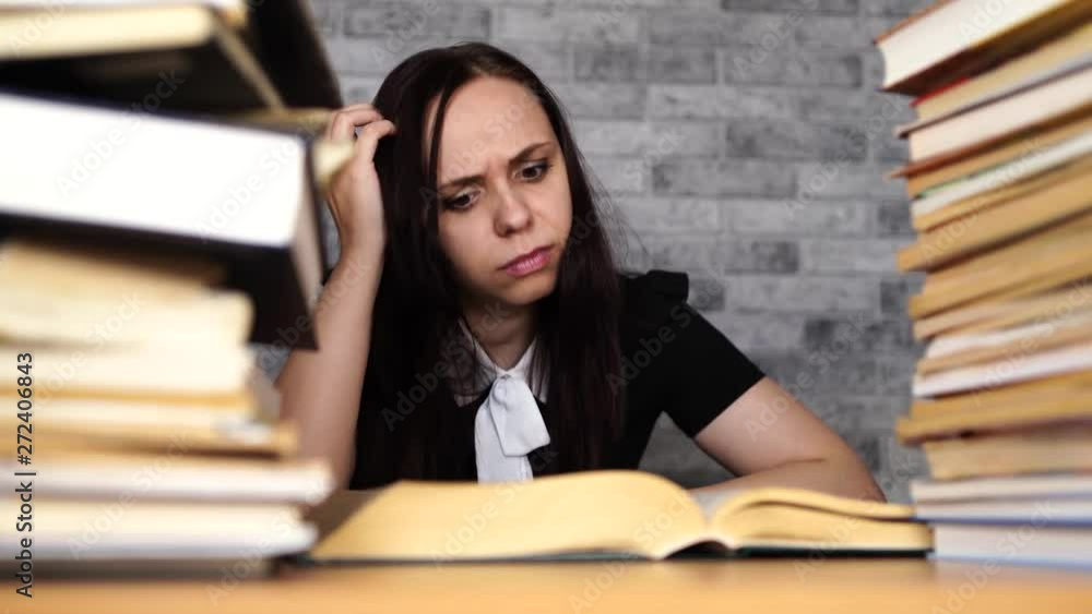 Woman student boring reading book at library with a lot of books in university. Student disheartened reading book for examination. Woman student boring reading book at library with a lot of books in university. Student disheartened reading book for examination.