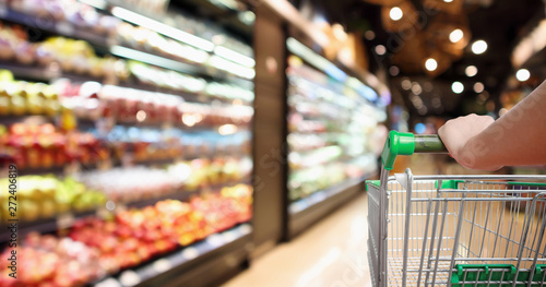 Fototapeta woman hand hold supermarket shopping cart with abstract blur organic fresh fruit