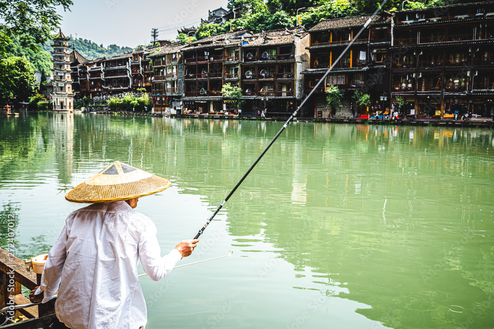 Chinese fisherman wearing an Asian conical hat and scenery of