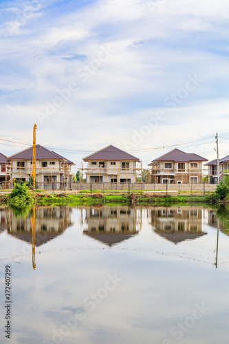 New house building reflection with water in lake at residential estate construction site with clouds and blue sky