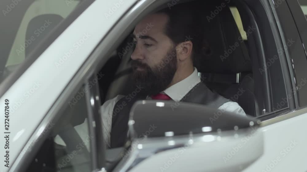 Successful man sitting in passenger compartment of the new vehicle inspects the interior of the newly purchased auto from the dealership. Car showroom. Advertising concept. Successful man sitting in passenger compartment of the new vehicle inspects the interior of the newly purchased auto from the dealership. Car showroom. Advertising concept.