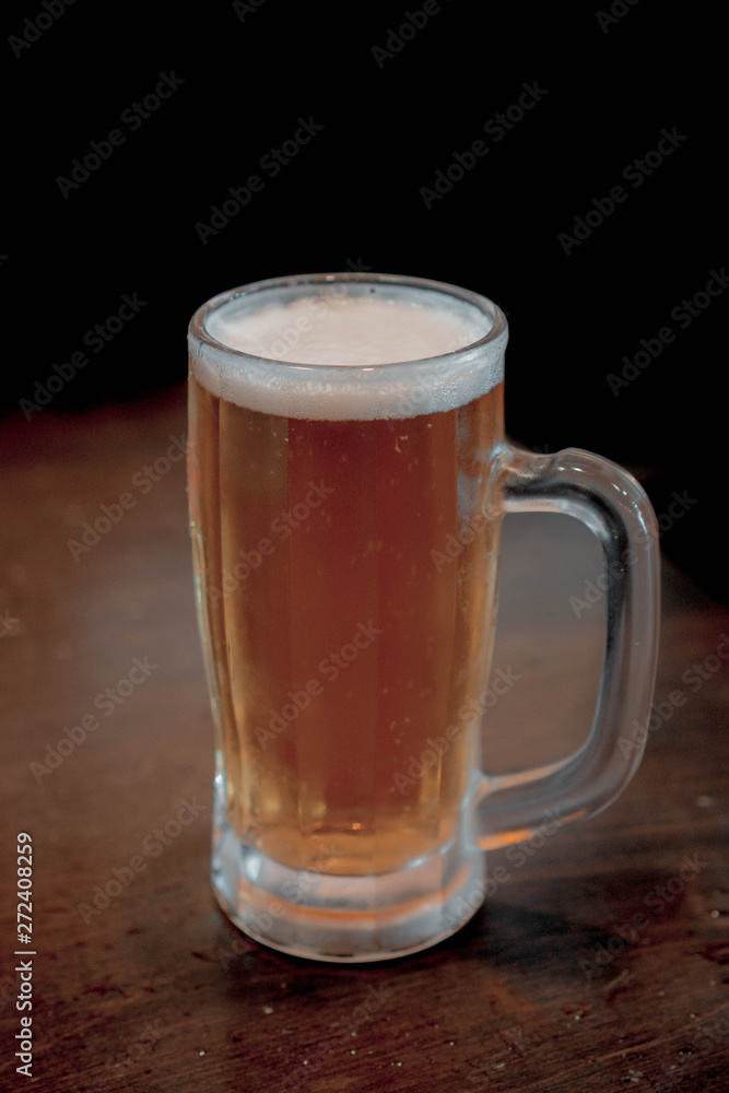 frosted mug filled with a golden amber ale beer on a wooden table. dark room frosted mug filled with a golden amber ale beer on a wooden table. dark room